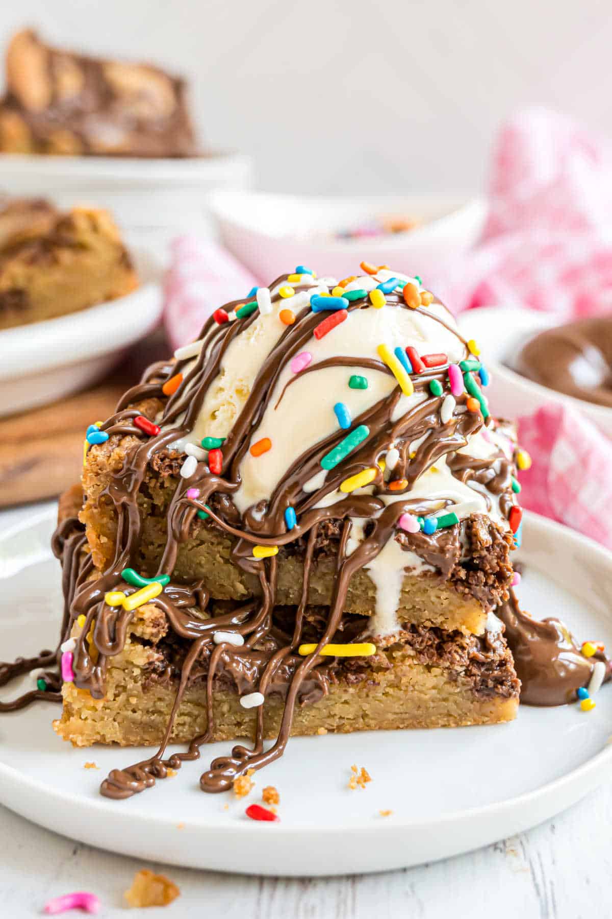 Two blondies topped with ice cream, sprinkles, and melted nutella.