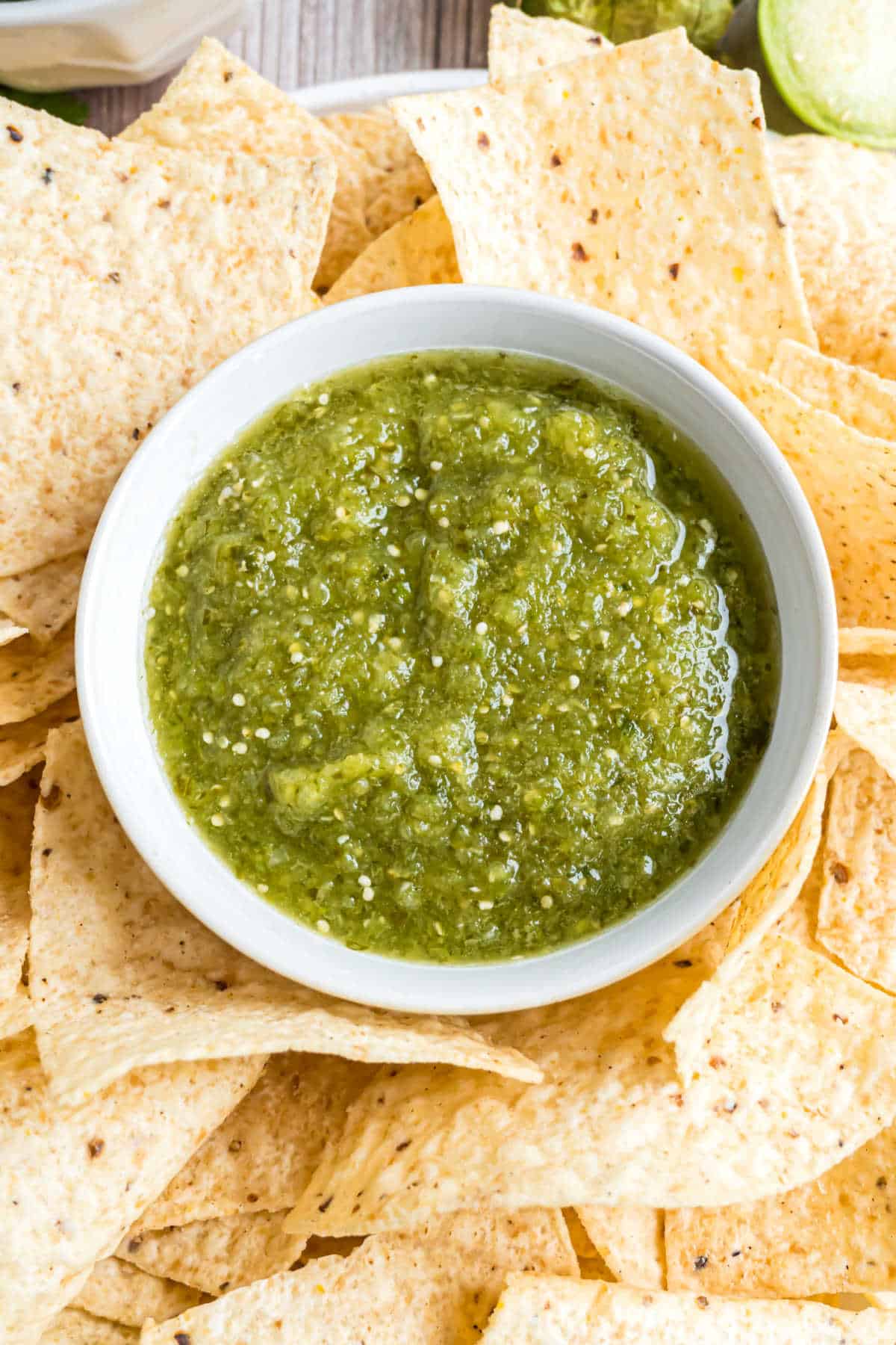 Bowl of green salsa with tortilla chips around it.