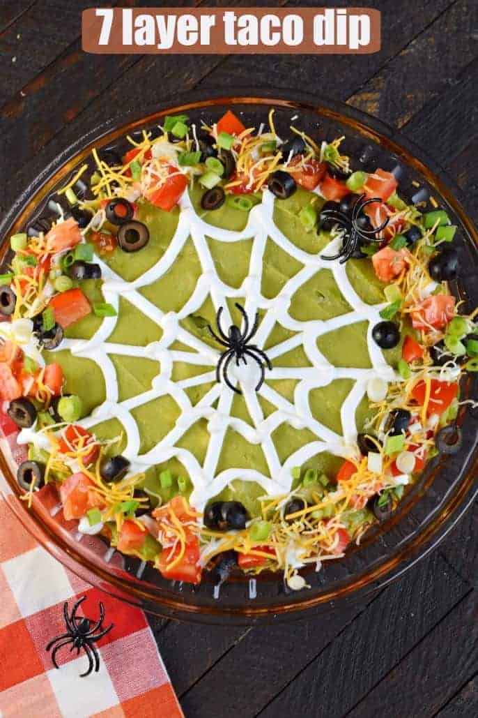 Halloween seven layer taco dip decorated with spider web made from sour cream.