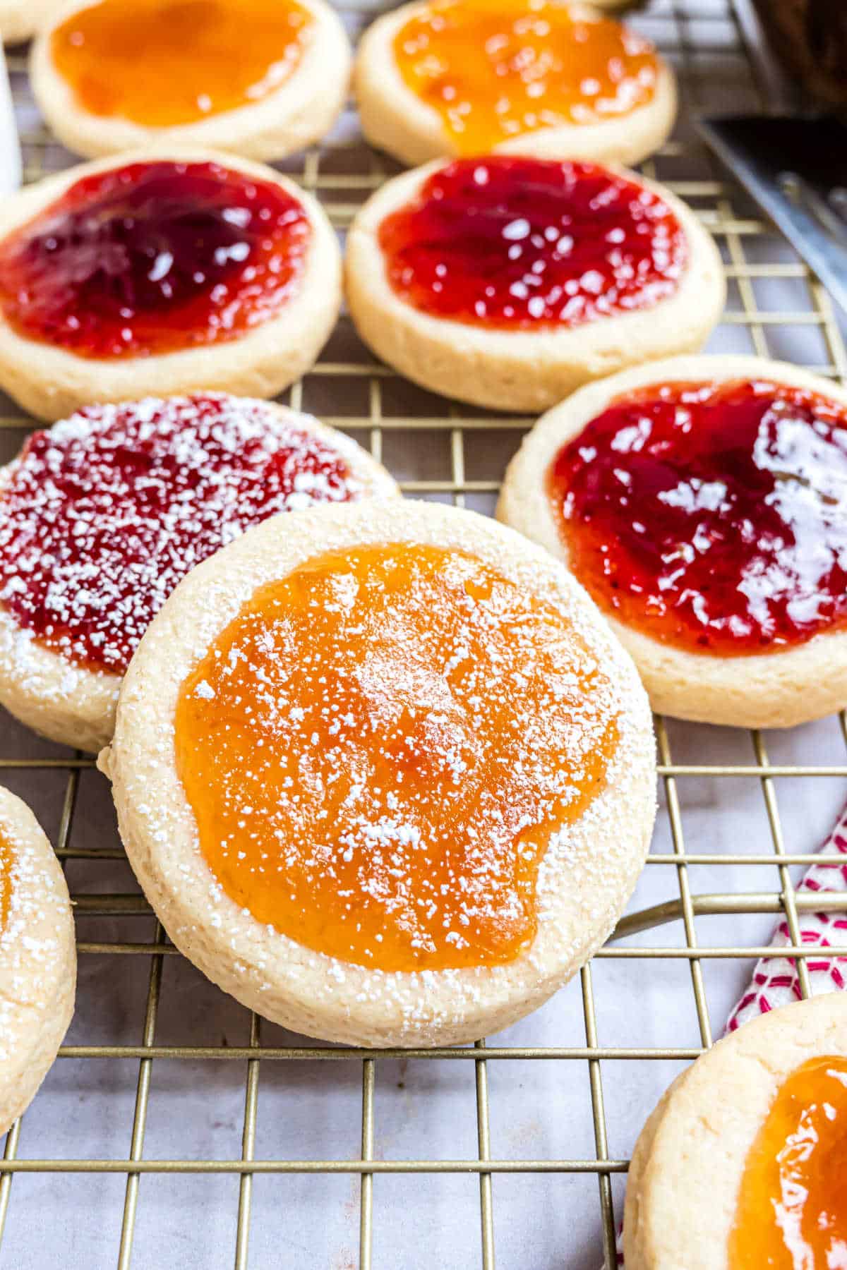 Soft cookies topped with fruit preserves and powdered sugar on a wire rack.