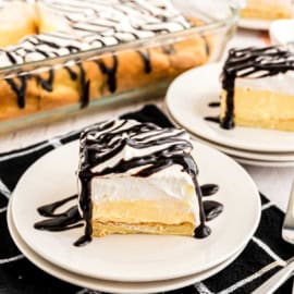 Slice of cream puff cake topped with chocolate syrup.
