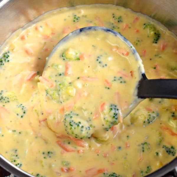 Cheesy broccoli soup being ladled out of pan.