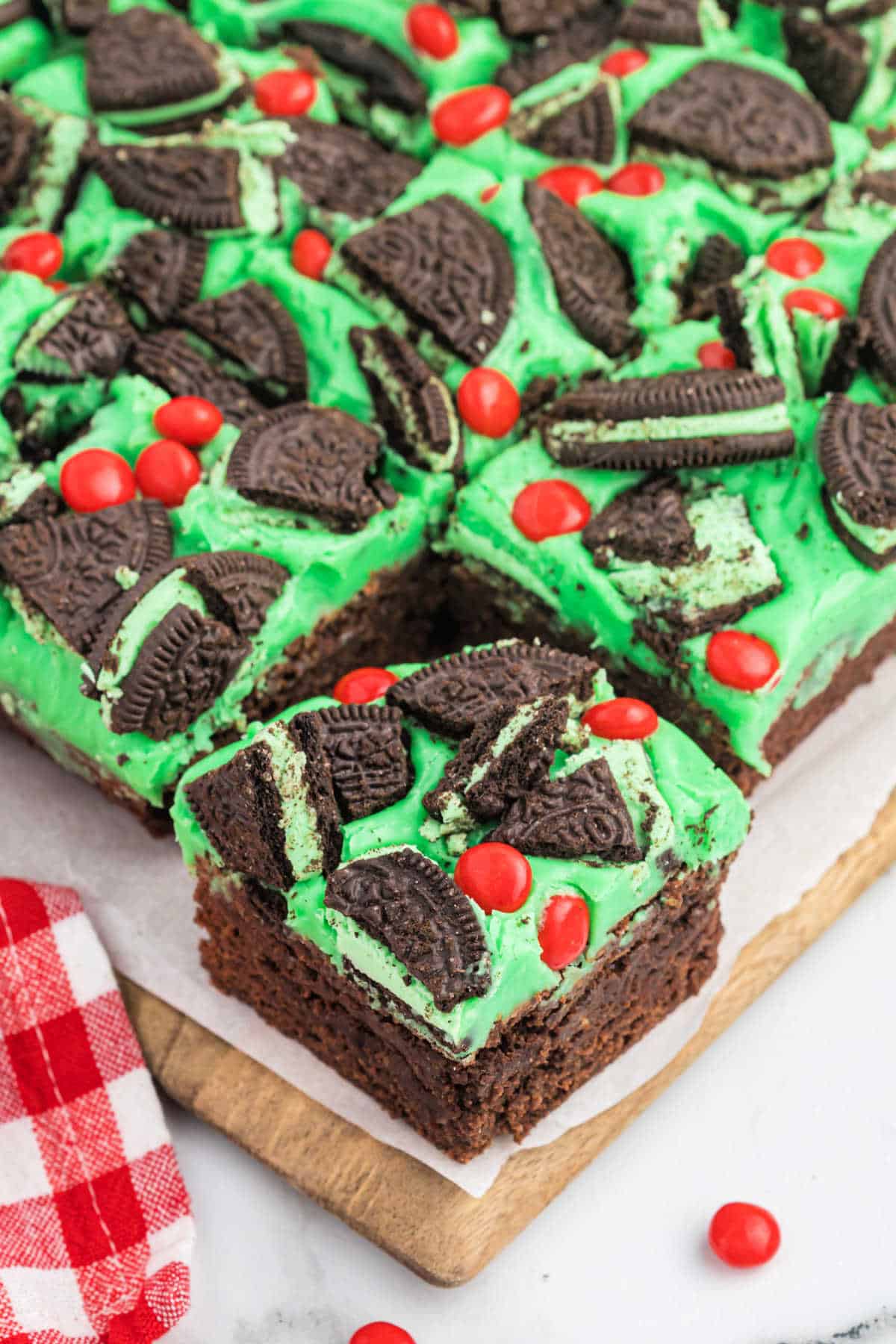 Grinch decorated brownies cut into squares on a wooden cutting board.