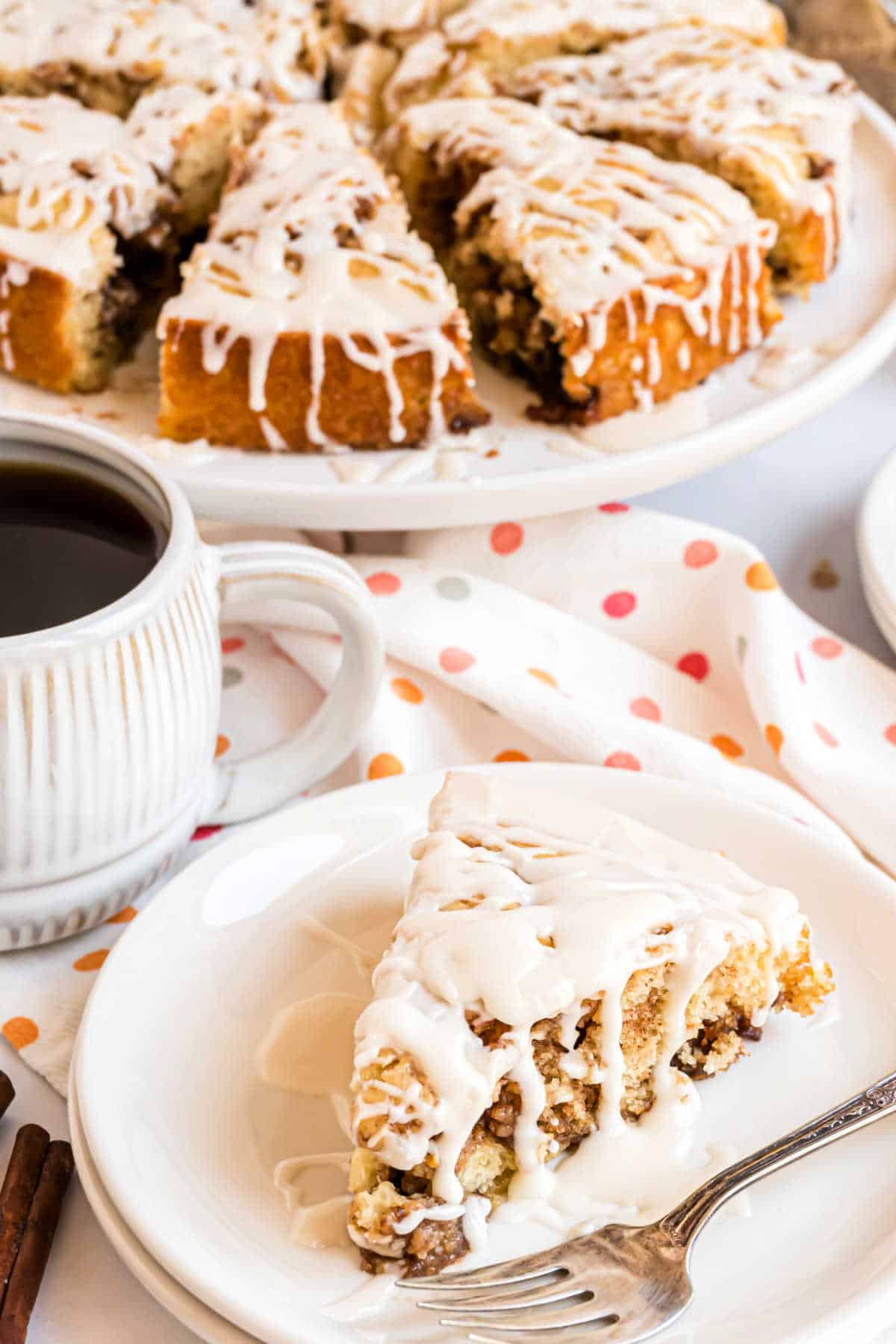 Slice of cinnamon roll cake with vanilla icing on a white plate.