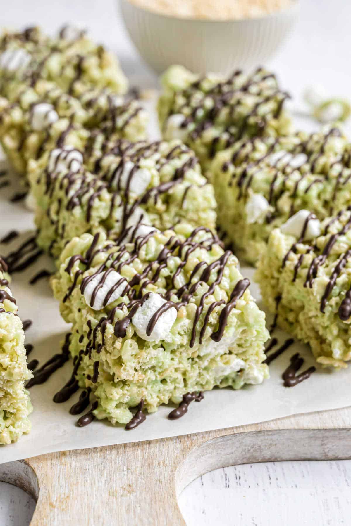 Pistachio krispie treats cut into squares on parchment paper and drizzled with dark chocolate.