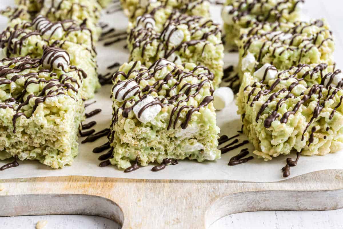 Squares of pistachio rice krispie treats and chocolate drizzle on parchment paper.