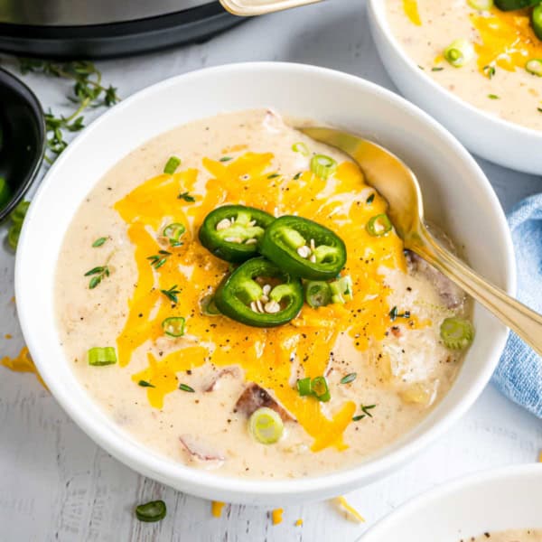 White bowl of potato soup with cheese, chives, and jalapenos on top.