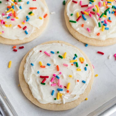 Frosted sugar cookies with sprinkles on a parchment paper lined cookie sheet.