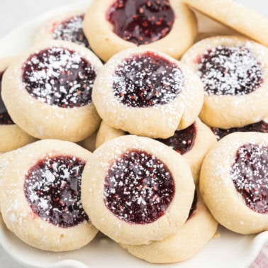 Stacks of jam thumbprint cookies on a white plate.