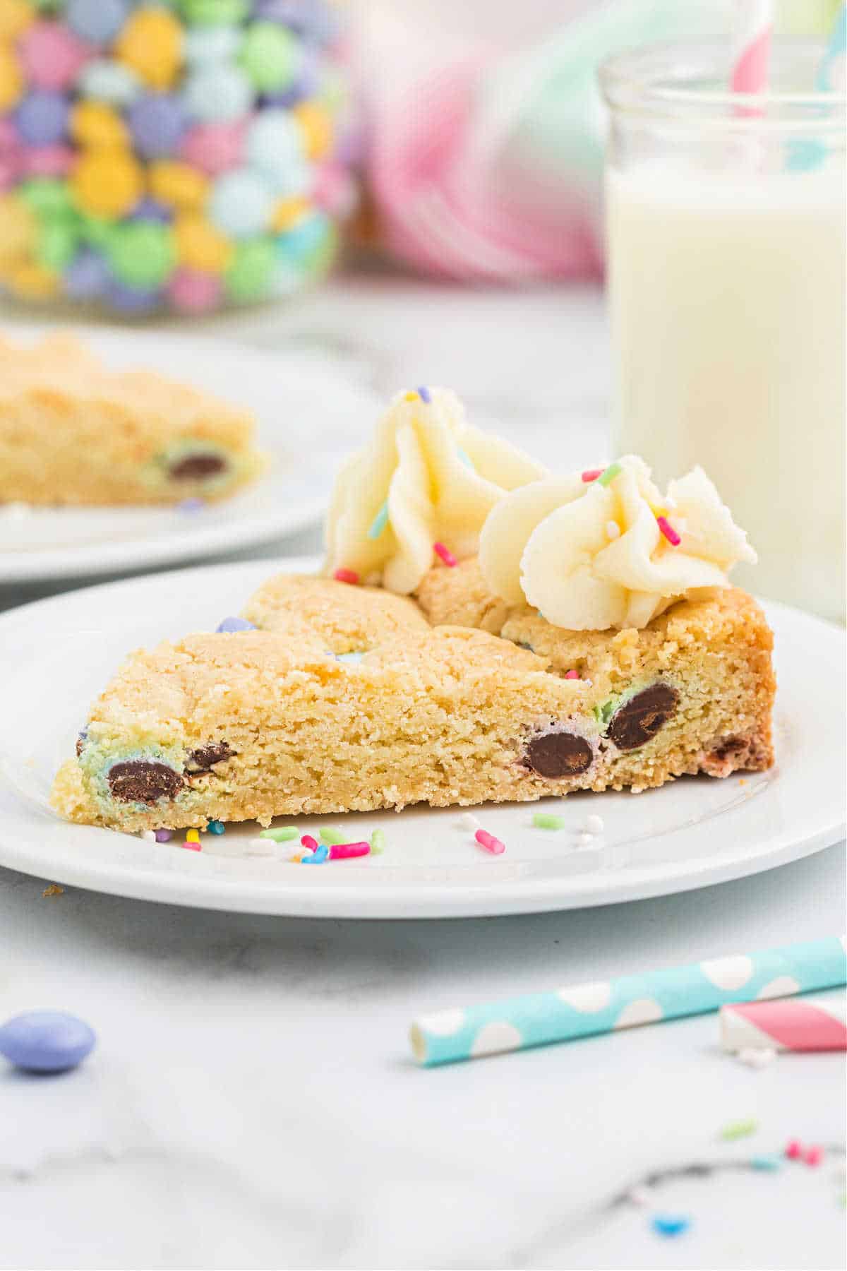 Slice of sugar cookie cake on a white plate with sprinkles.