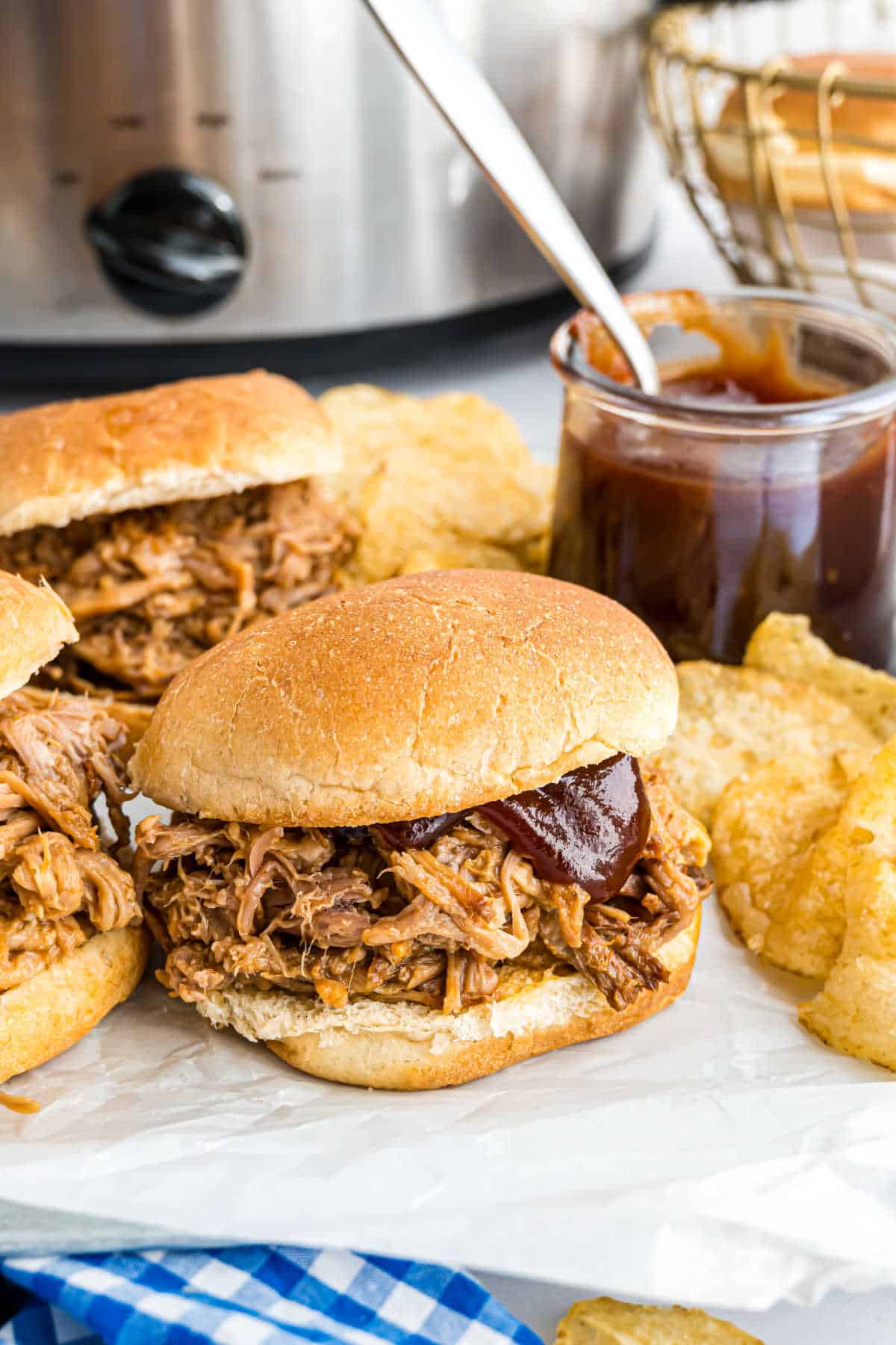 Pulled pork sandwiches with bbq sauce and potato chips on the side.