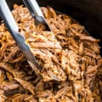 Shredded pork being lifted by tongs.