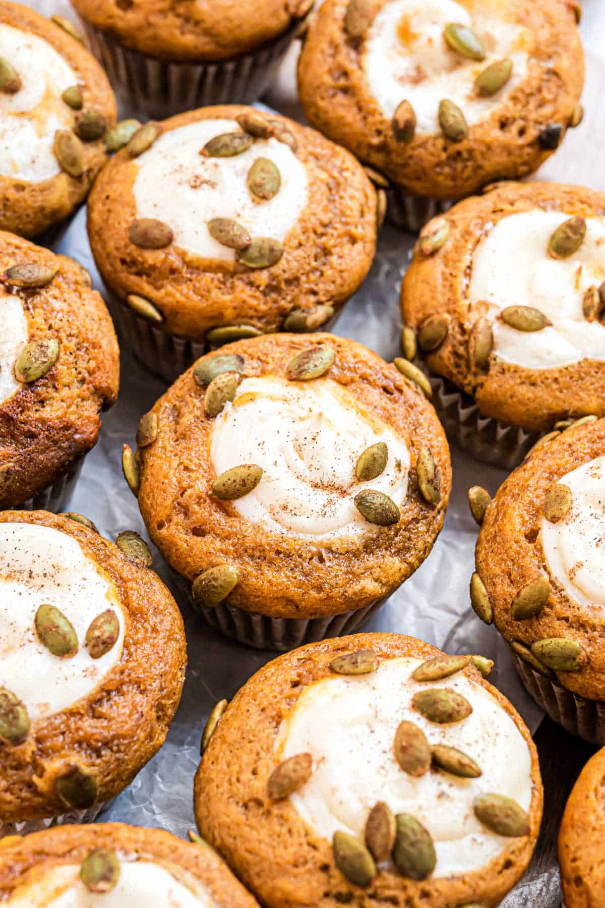 Pumpkin muffins with cream cheese cooling on counter.