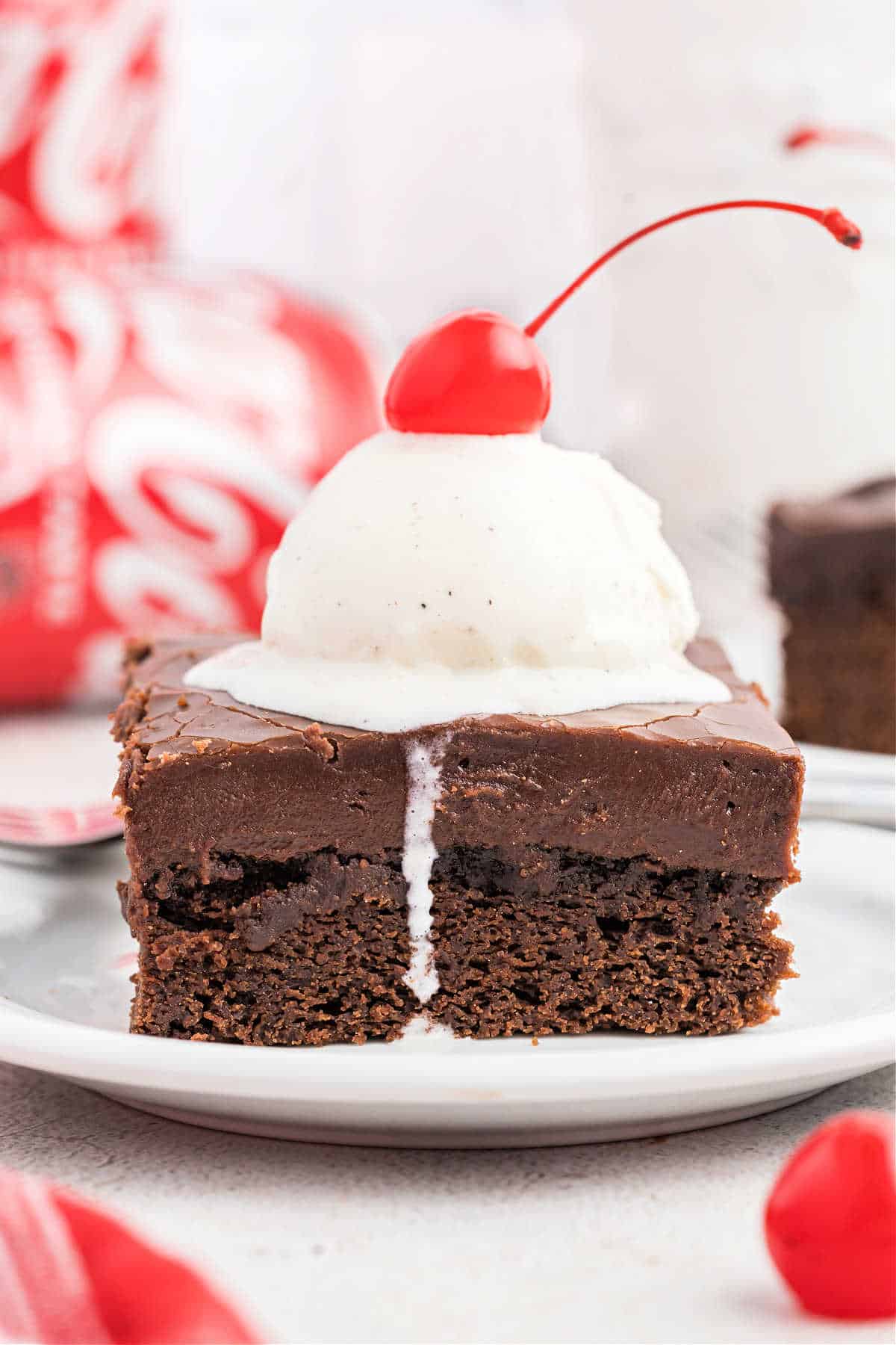 Slice of coca cola chocolate cake with vanilla icing on a white plate.