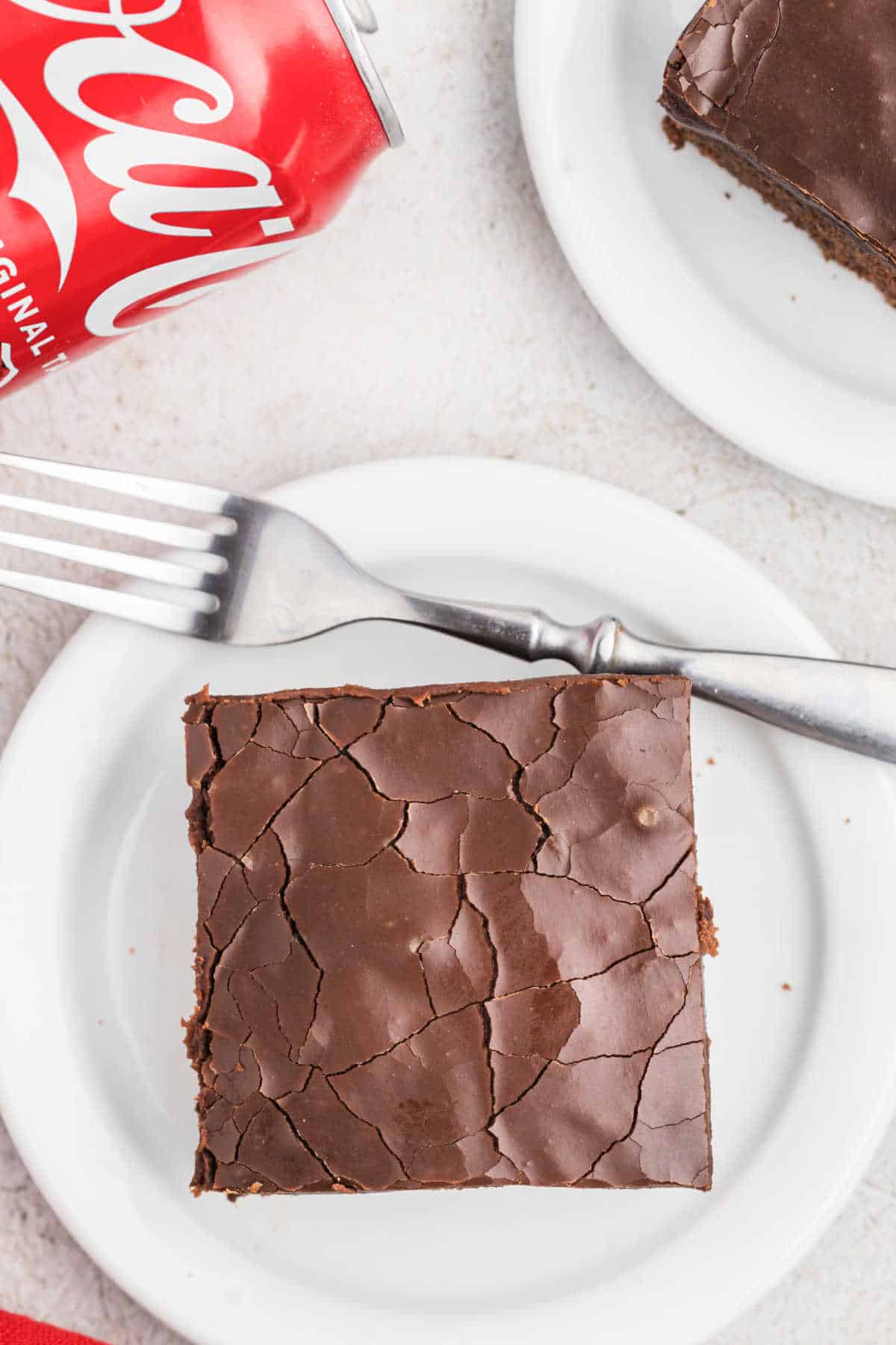 Slice of cocoa cola cake with chocolate icing on a white plate.