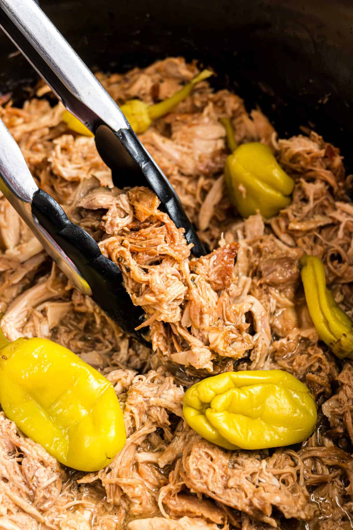 Shredded chicken a pepperoncinis in a crockpot with tongs.