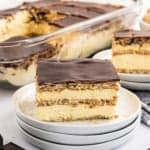 A slice of chocolate eclair cake rests on stacked plates, tempting you to discover the full chocolate eclair cake recipe hiding in the glass dish behind.