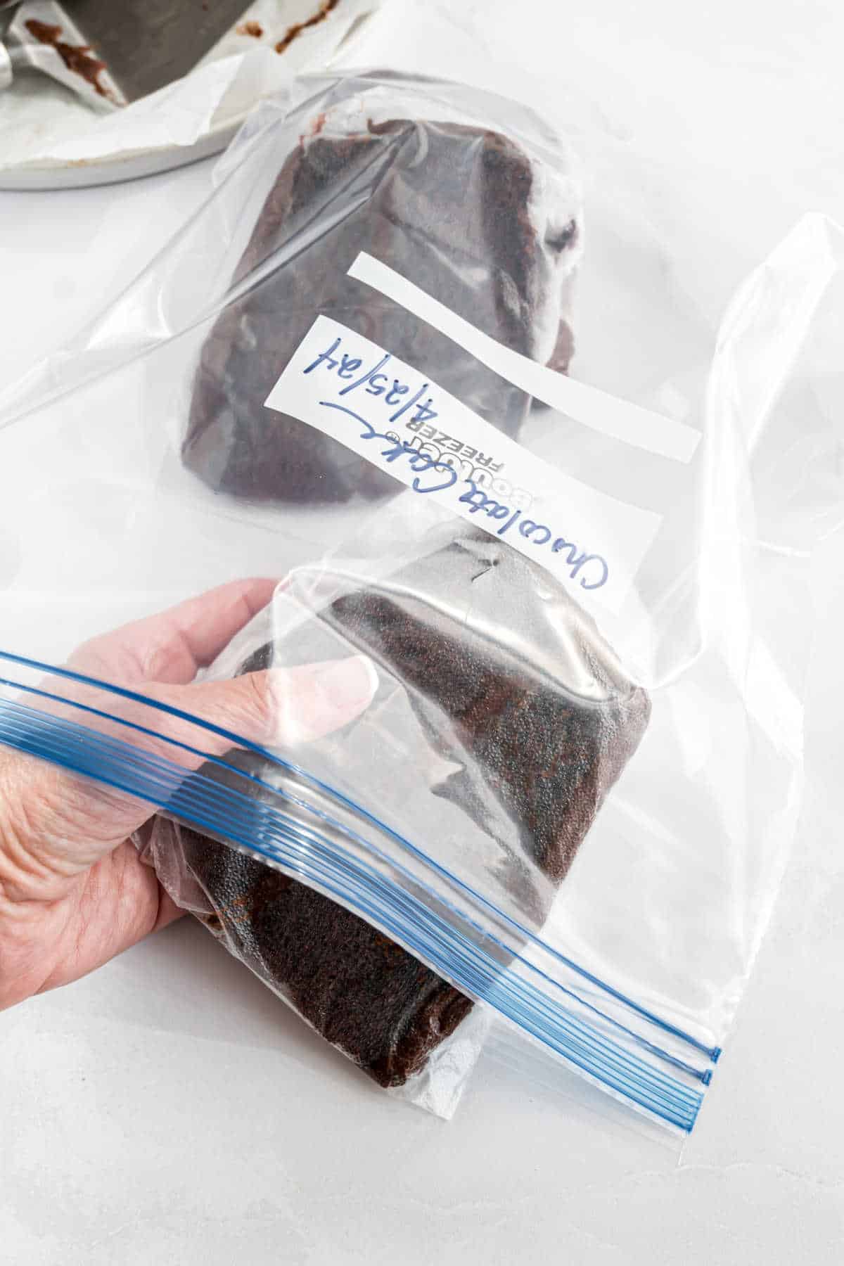 Chocolate cake slices being put into a ziploc freezer bag.