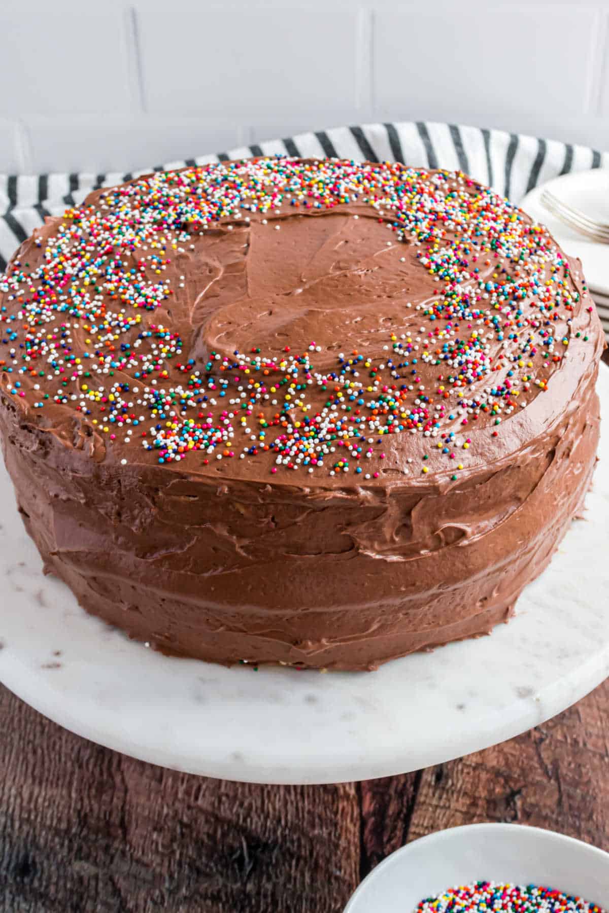 Chocolate frosted cake with sprinkles on a marble cake platter.