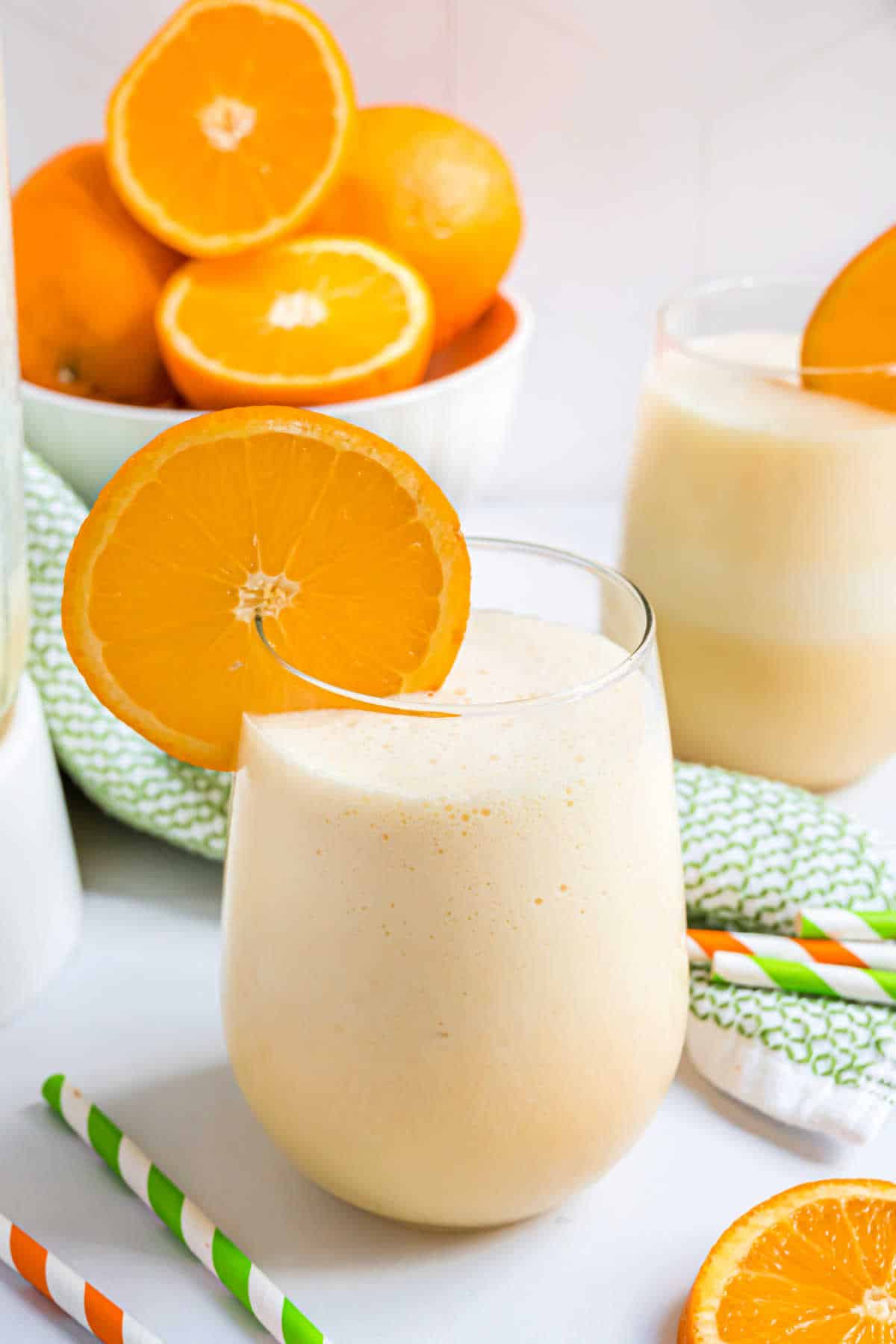 Orange julius in a stemless wine glass with an orange garnish.