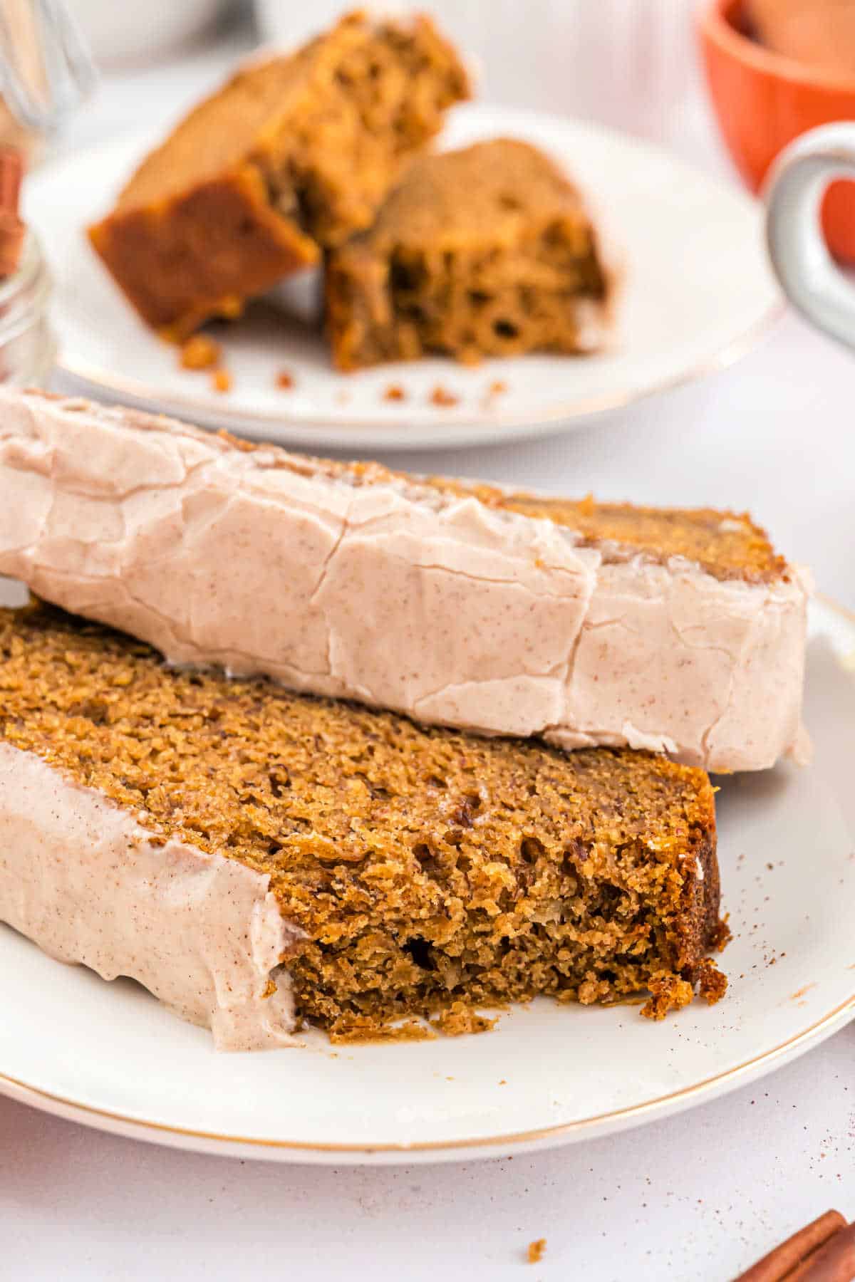 Two slices of frosted pumpkin banana bread on a plate with a bite taken out.