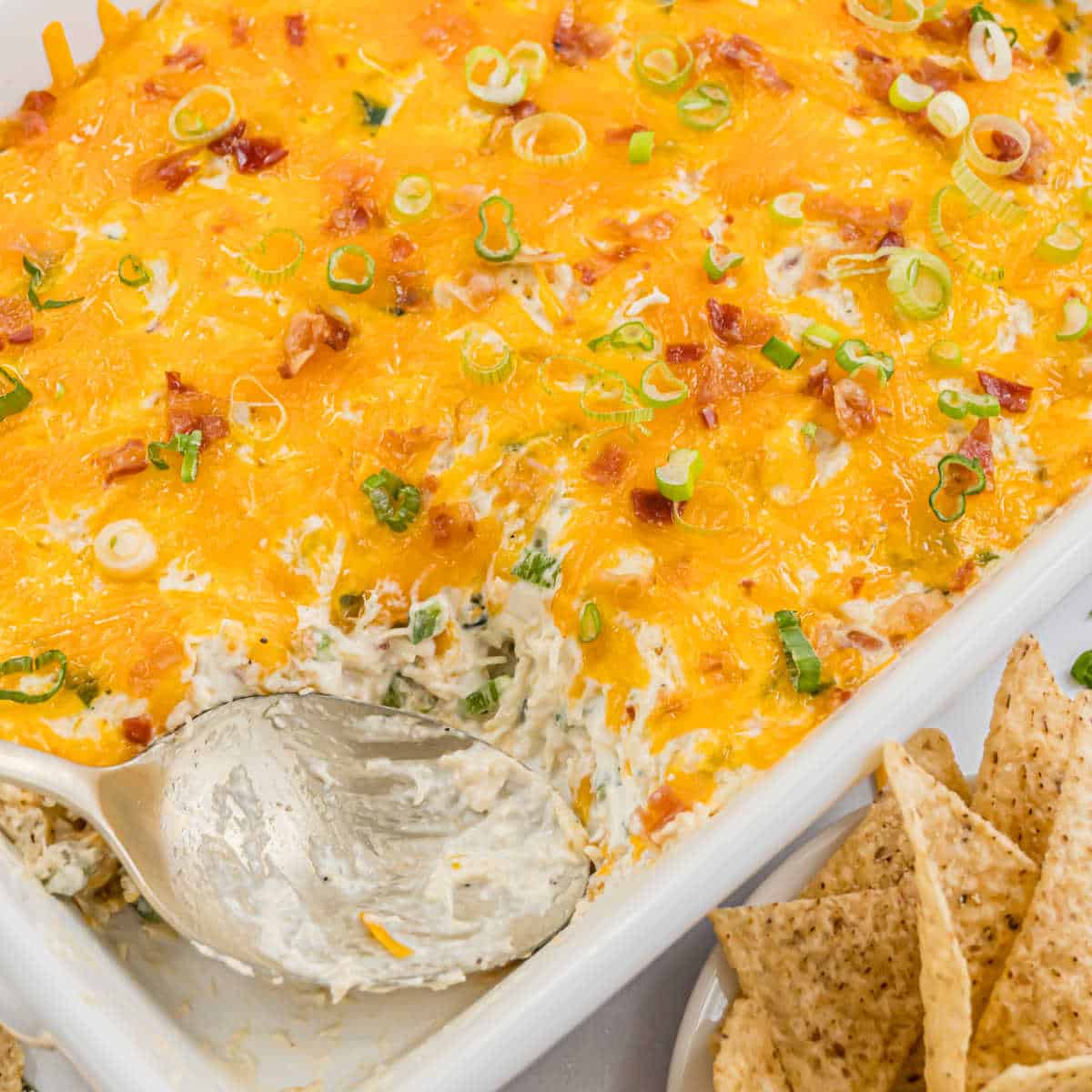 Baked cheesy dip with a hint of jalapeño popper chicken casserole flavor, topped with bacon bits and green onions, served with crispy tortilla chips.