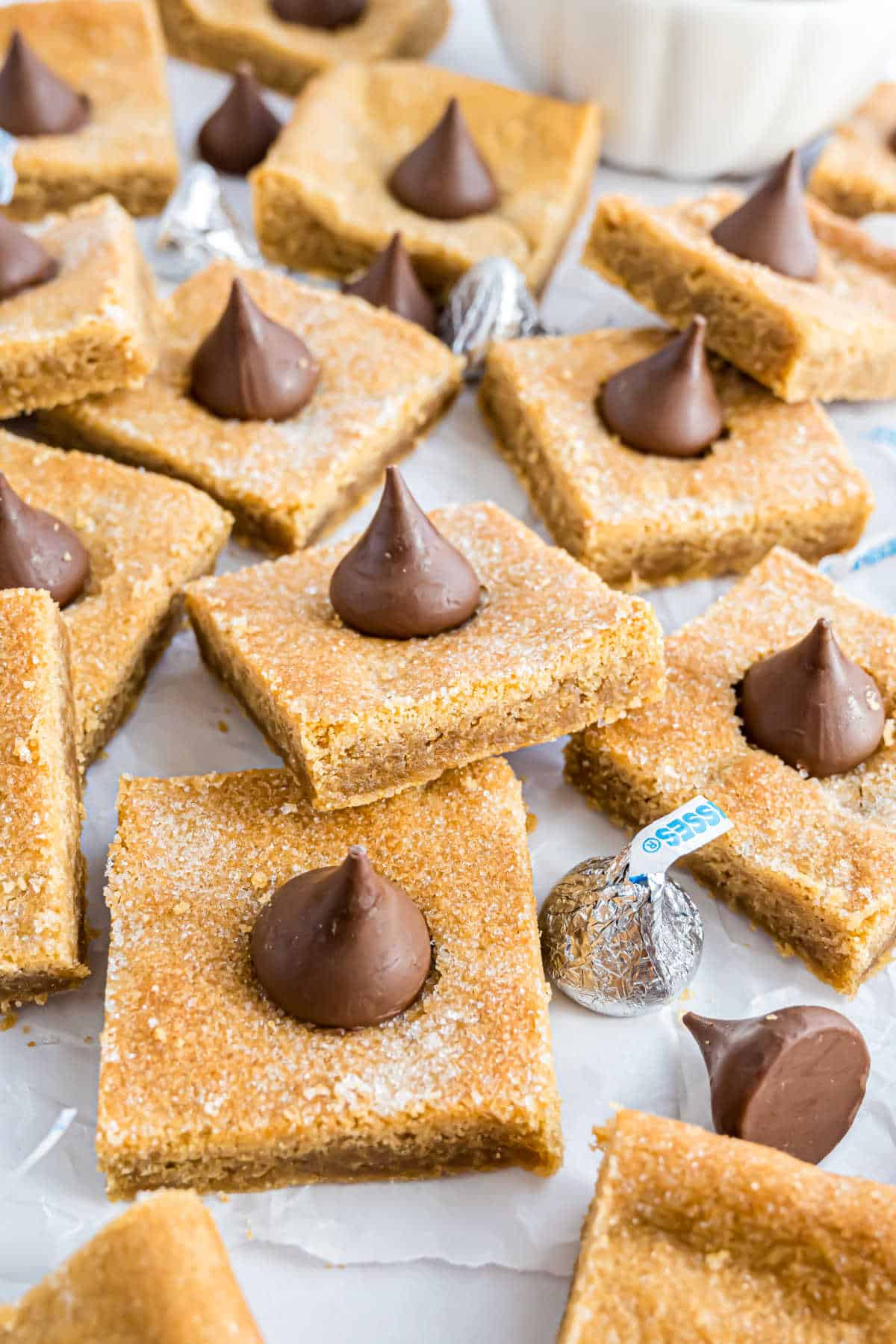 Squares of cut peanut butter blossom cookie bars on parchment paper.